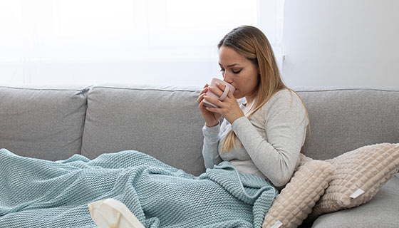 Woman with cold relaxing on a gray sofa while drinking tea